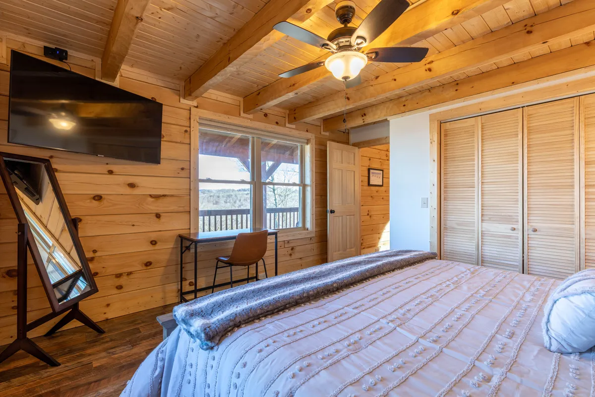 A king bedroom with a plush bed faces a window with a scenic view, complemented by a mirror and wall-mounted television. The space feels bright and inviting, perfect for unwinding after a day of adventure.