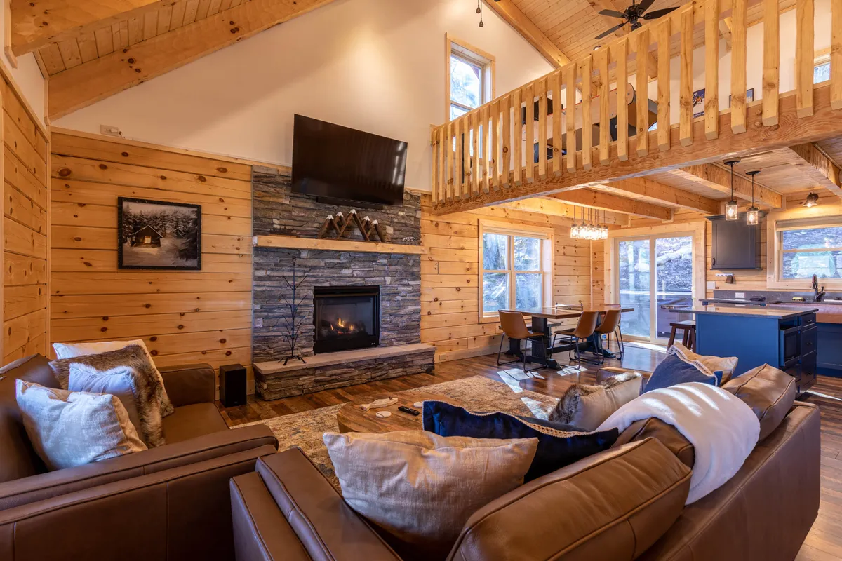 This interior shot centers on a cozy living area with a glowing fireplace, plush sofa, adjoining dining area, and a glimpse of the balcony beyond. The sunny atmosphere and thoughtful arrangement encourage both relaxing and socializing.