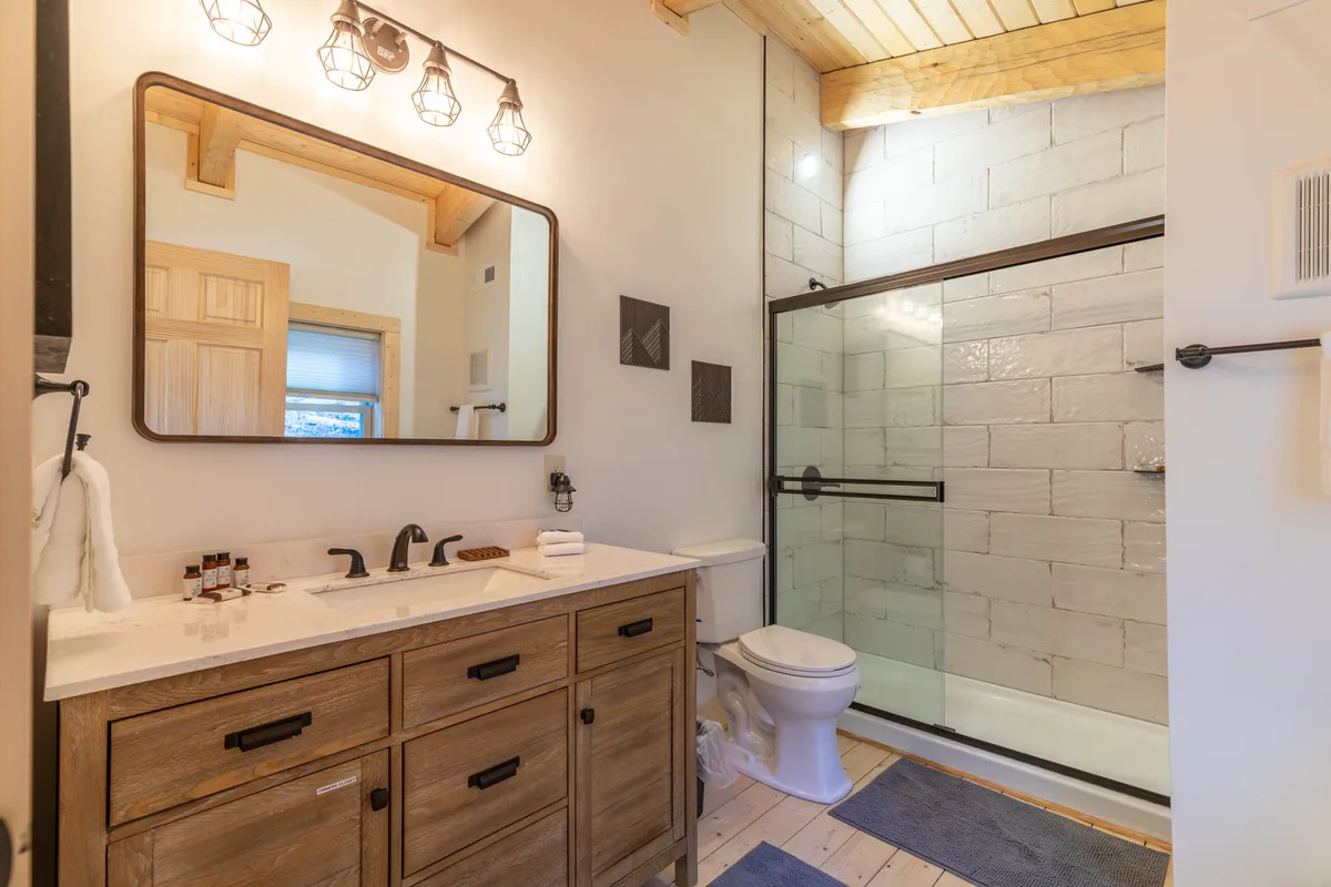 A modern bathroom with a vanity and large mirror, and a glass-enclosed shower. Sunlight illuminates the space, enhancing the clean, refreshing atmosphere ideal for self-care and relaxation.