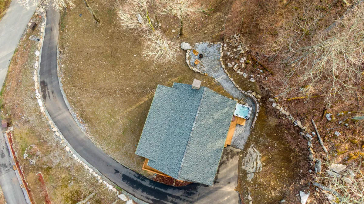 This image features a cabin with a winding driveway, a spacious deck, and a scenic mountain backdrop. The area is set up for outdoor gatherings and showcases the natural landscape around the property.