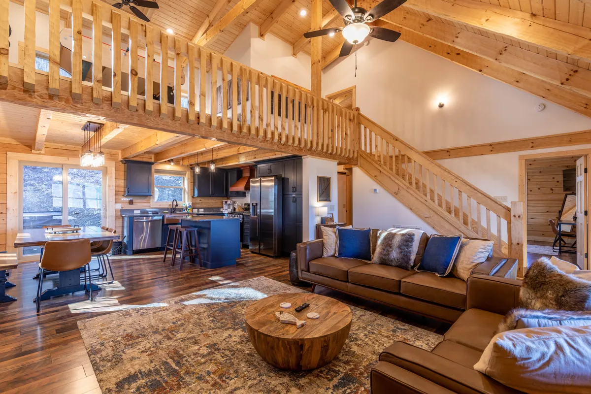 Showcasing exposed wooden beams, large windows with mountain views, a comfortable sofa, and a spacious dining table, this image conveys the welcoming, communal spirit of Ursa Minor’s main living area.