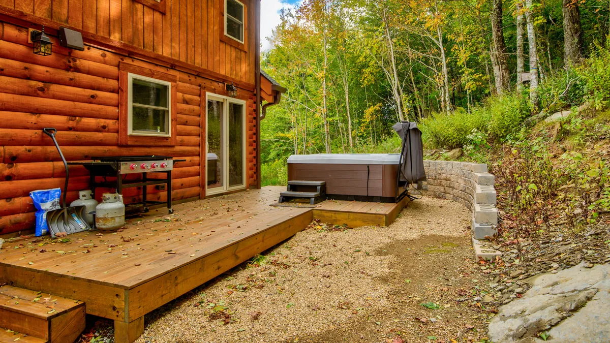 A wooden deck set amidst natural surroundings features a hot tub, grill, and tranquil woodland backdrop. The setup invites guests to enjoy a relaxing soak, host outdoor gatherings, or spot local wildlife, all within a private and scenic space.