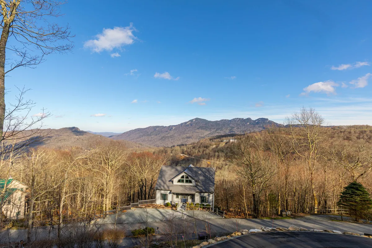 An inviting exterior view showing a house with a prominent mountain backdrop, tree line, driveway, and open spaces. Activities like hiking, family gatherings, and outdoor barbecues are suggested by the setting, and the tranquil mood is emphasized by the scenic surroundings.