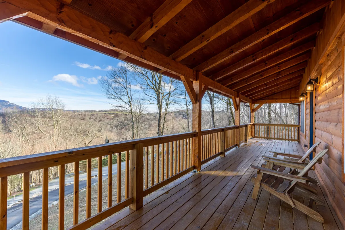 A tranquil exterior view featuring a wooden porch with rocking chairs and sweeping mountain vistas. The scene is bathed in soft natural light, surrounded by trees, emphasizing the peaceful mountain environment perfect for relaxation or inspiration during work breaks.