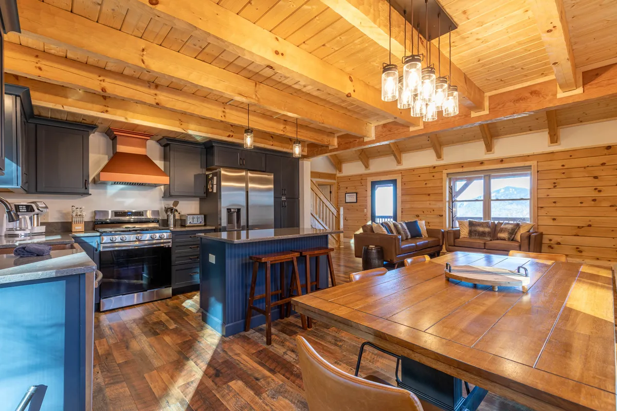 This image captures the heart of the open-concept main level, showcasing the kitchen island, spacious dining table, and living area, all bathed in natural light from large windows. The granite counters gleam, and cozy seating invites gatherings, while the fireplace in the background adds a warm, welcoming touch.